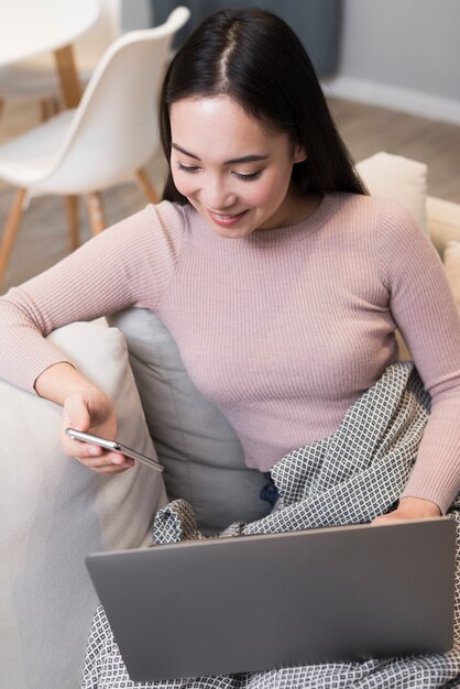 High angle of woman holding smartphone and laptop