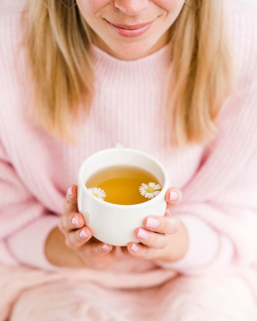 Foto gratuita donna dell'angolo alto che tiene tazza bianca con tè e fiori