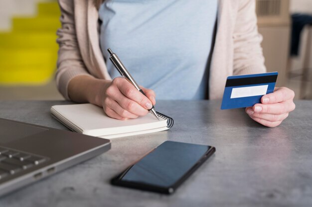 High angle of woman at home holding credit card and and writing in notepad