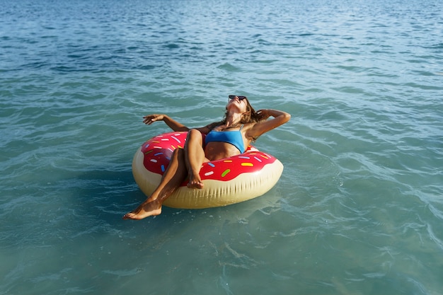 Женщина под высоким углом, лежащая на поплавке с пончиками