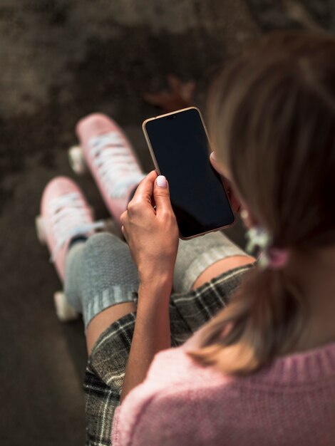 High angle of woman in roller skates holding smartphone