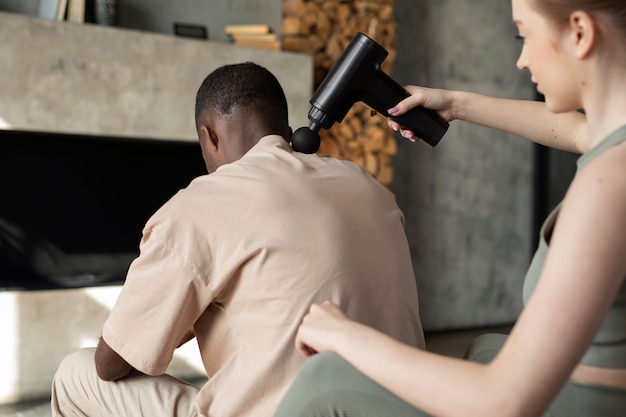 High angle woman using massage gun on man