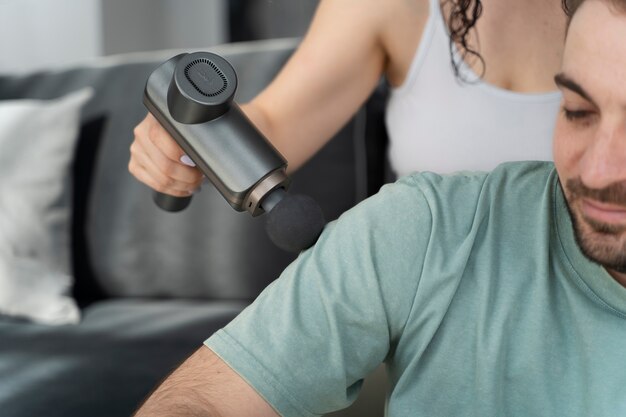 High angle woman using massage gun on man