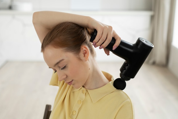 Free photo high angle woman using massage gun