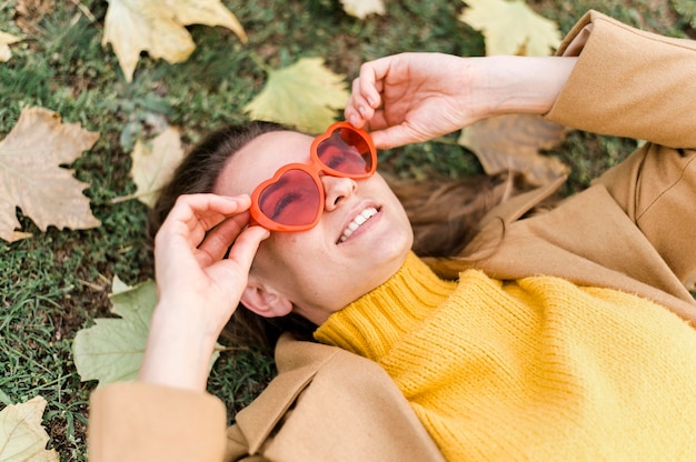 Женщина высокого угла в очках в форме сердца рядом с осенними листьями