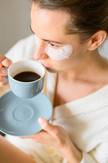 Free photo high angle of woman with eye patches drinking coffee