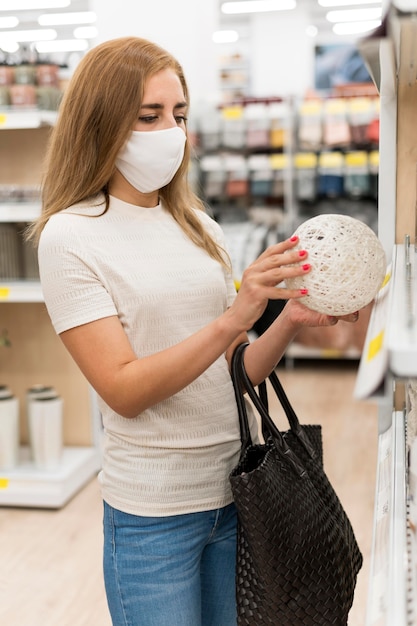 Женщина высокого угла с маской на покупках