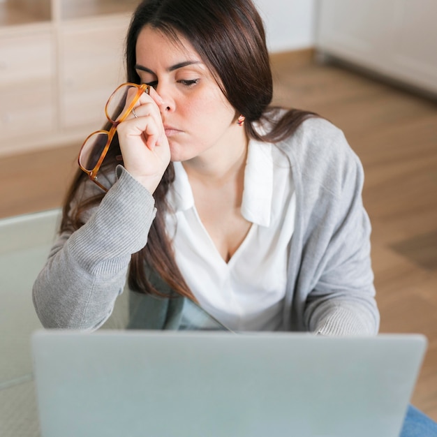 Free photo high angle woman working on laptop and holding glasses