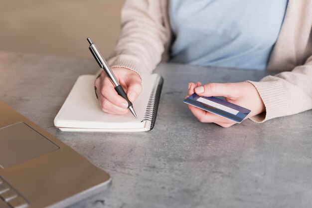 High angle of woman writing down on notebook while holding credit card