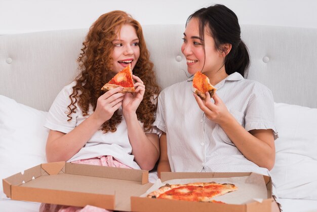 High angle women in bed eating pizza