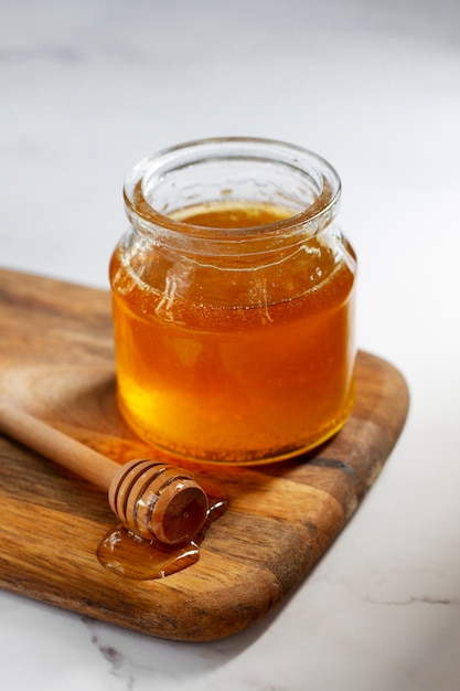 High angle of wooden honey dipper next to jar of honey