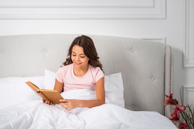 High angle young girl in bed reading