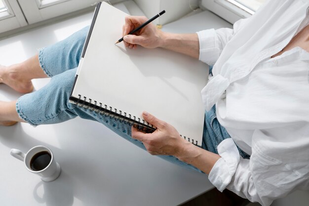 High angle of a young woman drawing at home near the window