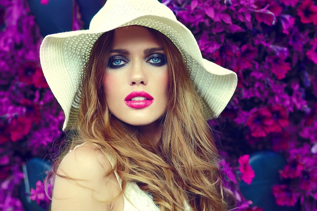 Free photo high fashion look.glamor closeup portrait of beautiful sexy stylish blond young woman model with bright makeup and pink lips with perfect clean skin in hat near summer flowers