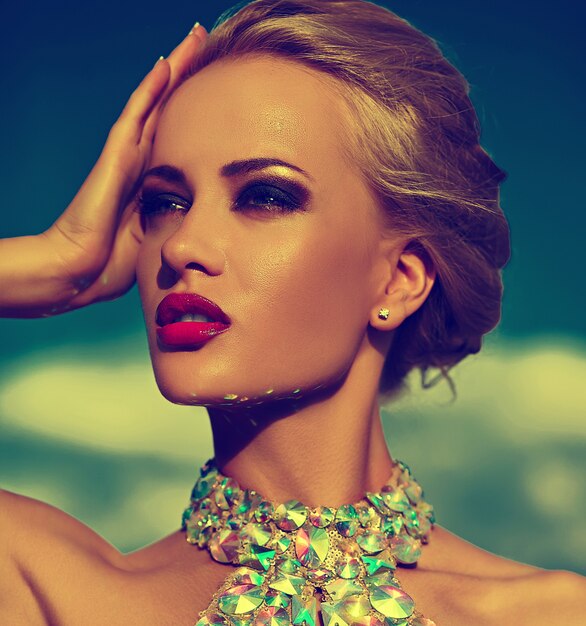 High fashion look.glamor closeup portrait of beautiful sexy stylish blond young woman model with bright makeup and red lips with perfect sunbathed clean skin with jewelery outdoors in vogue style in e