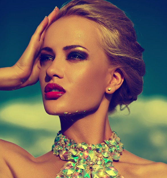 High fashion look.glamor closeup portrait of beautiful sexy stylish blond young woman model with bright makeup and red lips with perfect sunbathed clean skin with jewelery outdoors in vogue style in e
