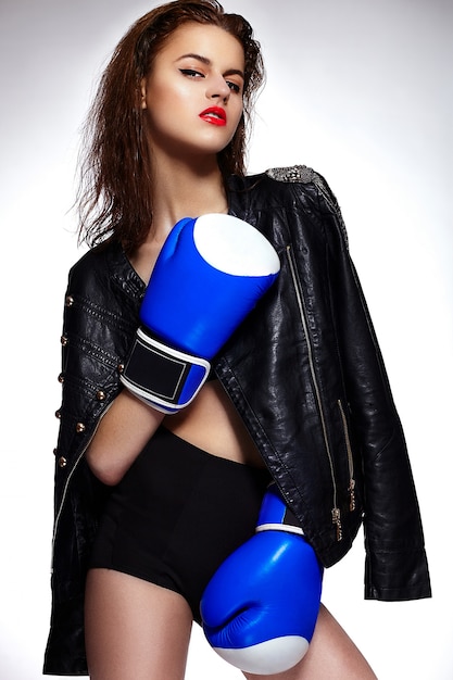 High fashion look.glamor closeup portrait of beautiful sexy stylish brunette boxing Caucasian young woman model with bright makeup, with red lips in blue boxing mitts in studio