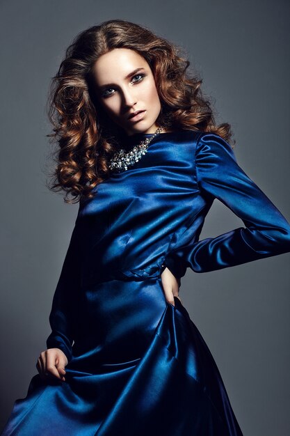 High fashion look. glamor portrait of beautiful stylish brunette Caucasian young woman model with bright makeup, with healthy curly hair in bright blue dress