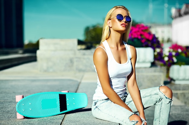 High fashion look.glamor stylish sexy beautiful young blond  model girl in summer bright casual hipster clothes with skateboard behind blue sky in the street