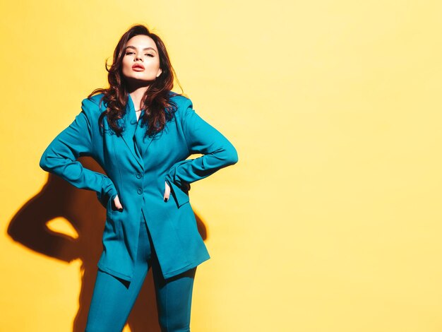 High fashion portrait of young beautiful brunette woman wearing nice trendy blue suit Sexy fashion model posing in studio Fashionable female isolated on yellow