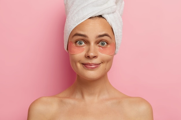 High resolution. Headshot of beautiful surprised young woman with healthy fresh skin, wears anti wrinkles patches under eyes, stands bare shoulders, looks straightly, visits spa center