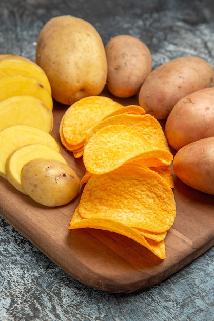 High resolution photo of crispy chips and uncooked potatoes on wooden cutting board on gray table