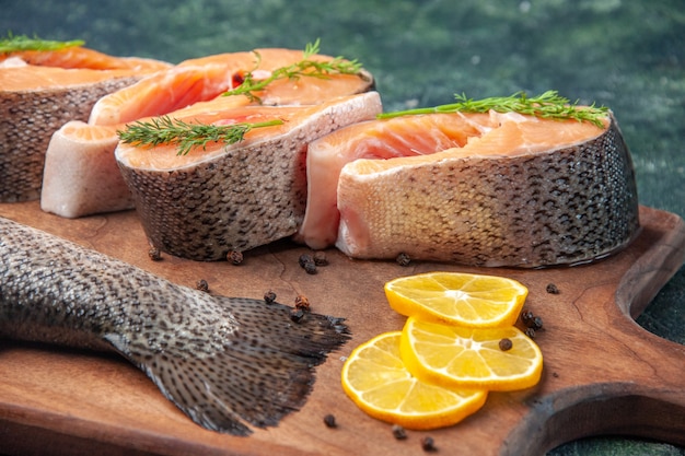 High resolution photo of fresh raw fishes lemon slices greens pepper on wooden cutting board on dark mix colors table