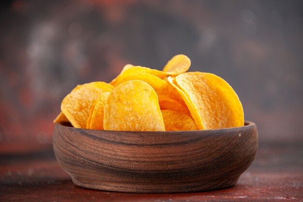High resolution photo of homemade delicious crispy potato chips in a small brown bowl on dark background