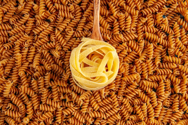 High resolution photo of various raw Italian pastas lined up in a row and wooden spoon