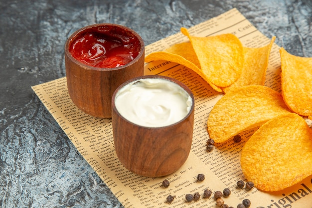 Free photo high resolution view of delicious homemade chips and pepper bowl mayonnaise ketchup on newspaper on gray table