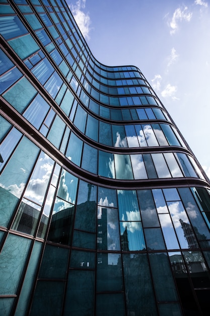 A high rise building in a glass facade with the reflection of the surrounding buildings