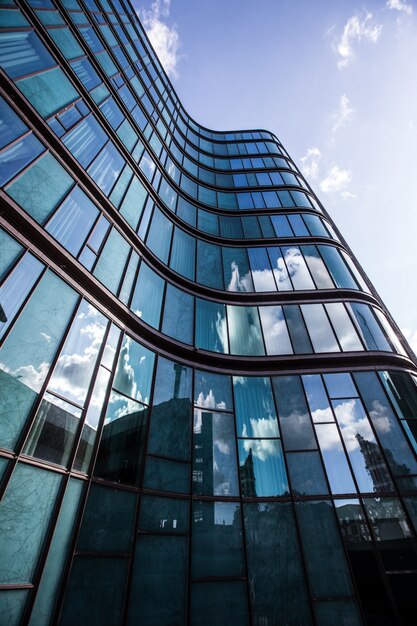 A high rise building in a glass facade with the reflection of the surrounding buildings