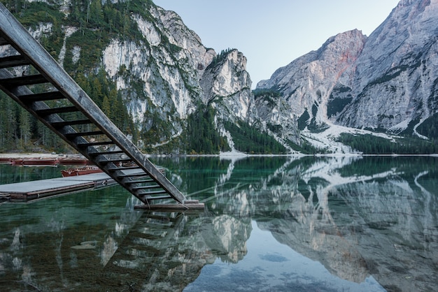 High rocky mountains reflected in Braies lake with wooden stairs near the pier in Italy