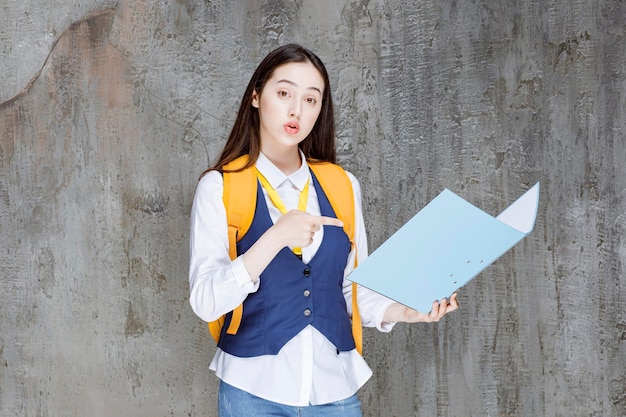 Ragazza del liceo con lo zaino giallo e la cartella che punta. foto di alta qualità