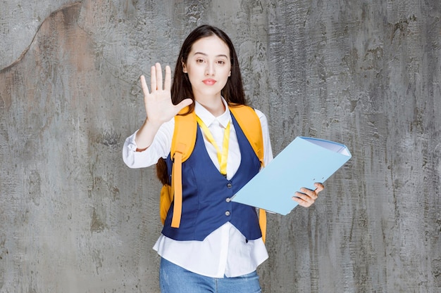 Free photo high school girl with yellow backpack and folder showing stop sign. high quality photo