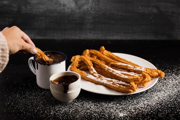 High view churros on a plate with mugs of sweet chocolate