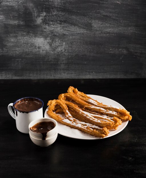 High view fried churros on a plate with mugs of chocolate