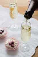 Free photo high view white wine glasses and bottle with cupcakes