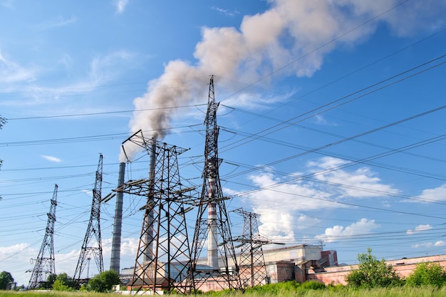 High voltage electric pylons against coal power plant high pipes with black smoke moving upwards polluting atmosphere. production of electrical energy with fossil fuel concept