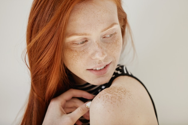 Highly-detailed shot of tender and cute teenage female with shy faint smile, loose ginger hair and and clean heathy skin looking over her shoulder Free Photo