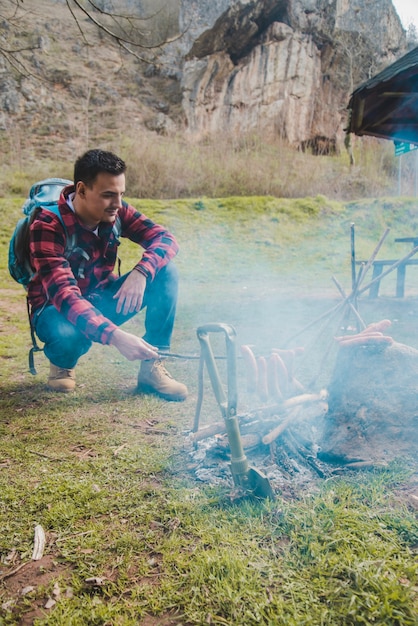 Free photo hiker by the fire preparing sausages