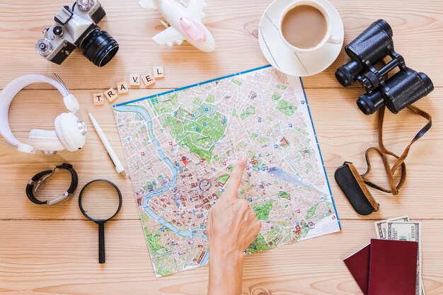 Hiker pointing at location on map with cup of tea and traveler accessories on wooden background