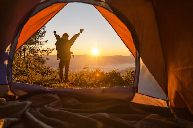 Hiker stand at the camping front orange tent and backpack in the mountains