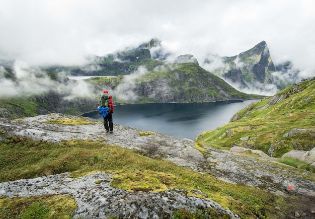 Hiker стоя около озера в горах Lofoten в туманный день