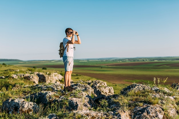 Hiker, стоящий на скале, смотрящий в бинокль