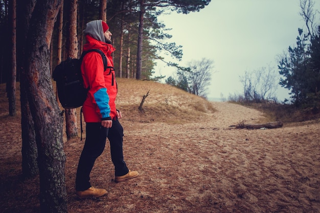 Путешественник стоит на песчаной дорожке за деревом