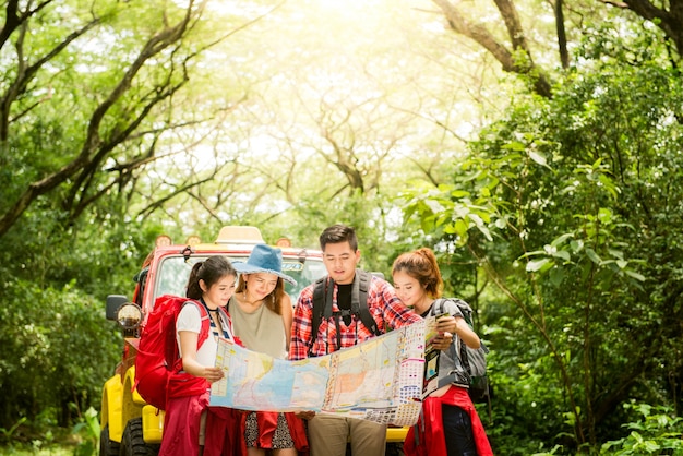 Hiking - hikers looking at map. Couple or friends navigating together smiling happy during camping travel hike outdoors in forest. Young mixed race Asian woman and man.