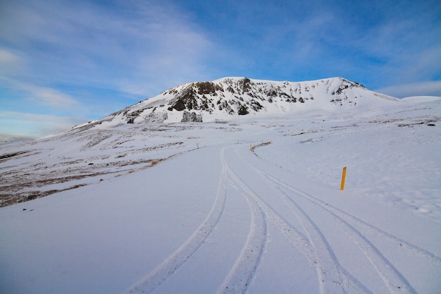 アイスランドの冬の間、日光と青い空の下で雪に覆われた丘