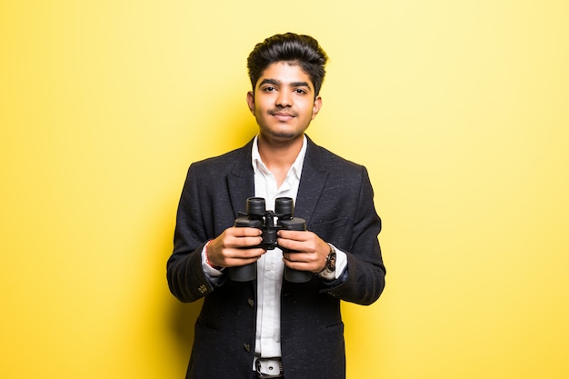 Hindu young man with binoculars isolated on yellow wall