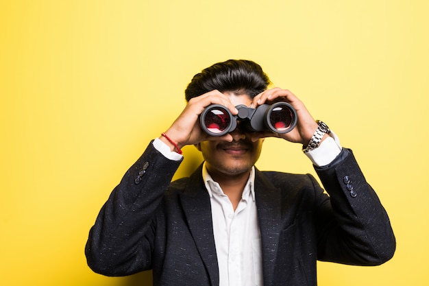 Hindu young man with binoculars isolated on yellow wall